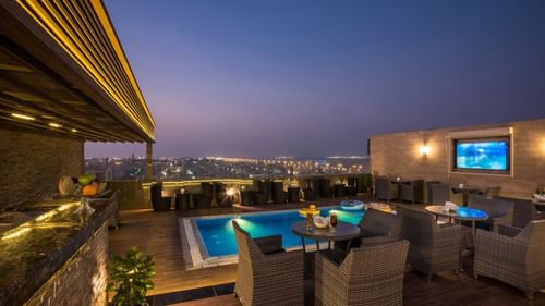 Modern rooftop pool with glowing lights by a stylish bar area under a night sky at Naviti By Warwick Dammam