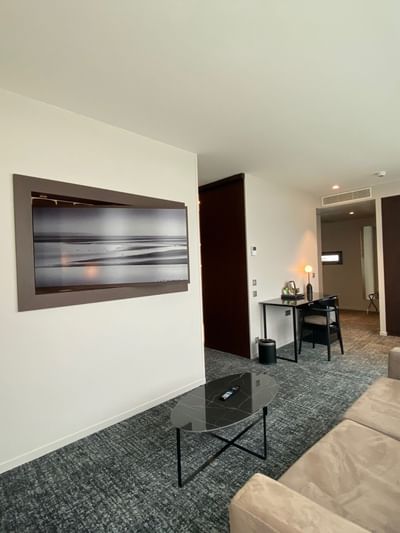 Suite moderne avec canapé, table basse, TV murale, bureau et chambre à coucher adjacente.