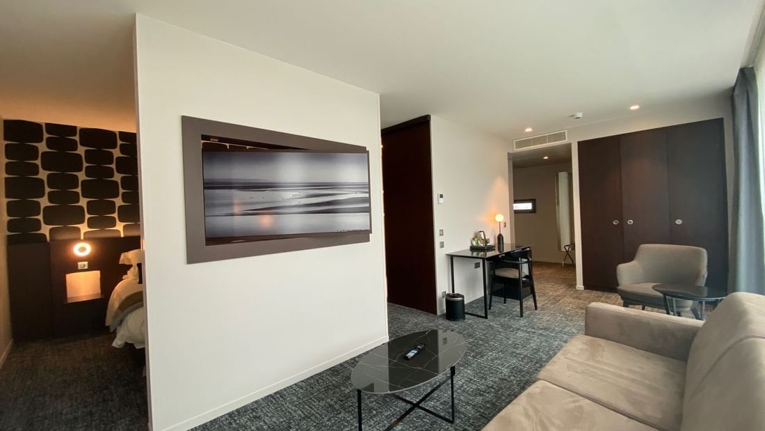 Suite moderne avec canapé, table basse, TV murale, bureau et chambre à coucher adjacente.
