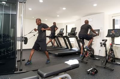 Men exercising on treadmills, bikes, and cable equipment by bright windows in the fitness center at Hotel Saint Clair