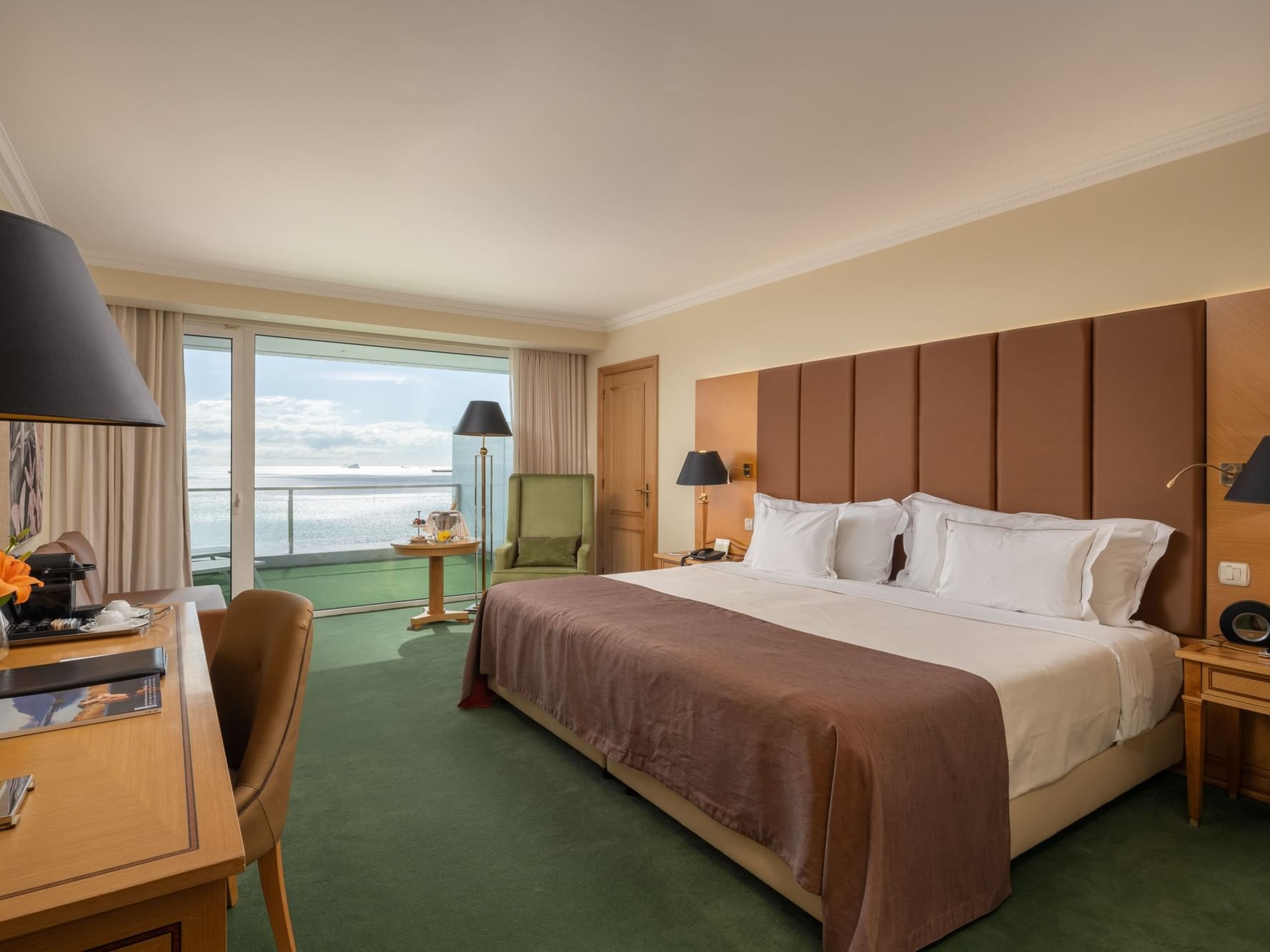 Quarto de hotel com cama grande, mesa, cortinas e vista para o mar.