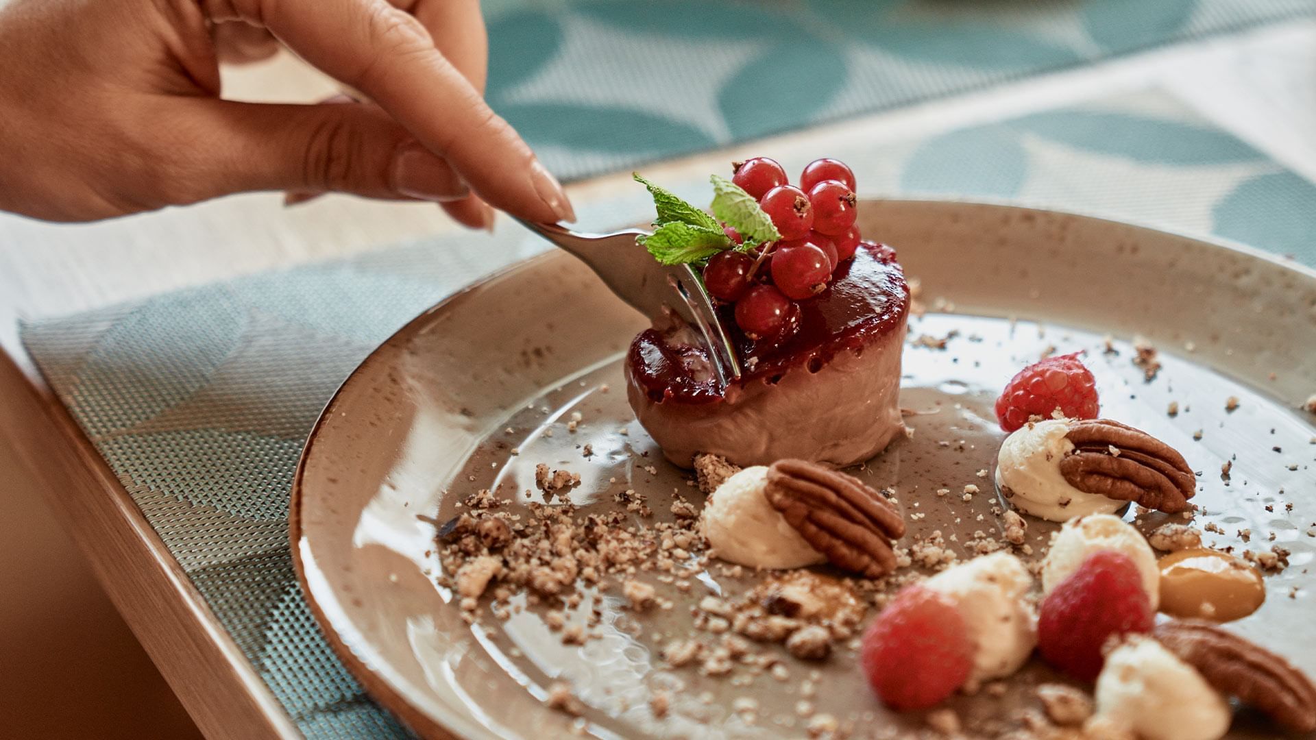 Eine Hand hält eine Gabel über einem Dessertteller mit Schokoladenkuchen, Beeren und Nüssen.