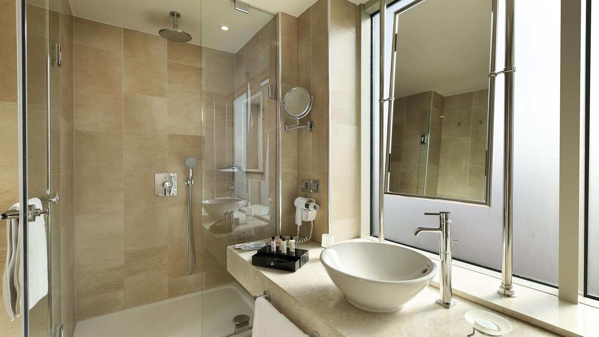 A modern bathroom with a glass shower, a white sink, a mirror, and a large window showing an outdoor view in Deluxe Room at Titanic Port Bakırköy