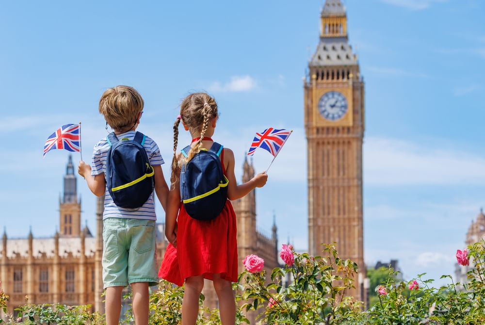 Children holding British flags by a rose bush, with Big Ben in the background at The Capital Hotel, Apartments and Townhouse