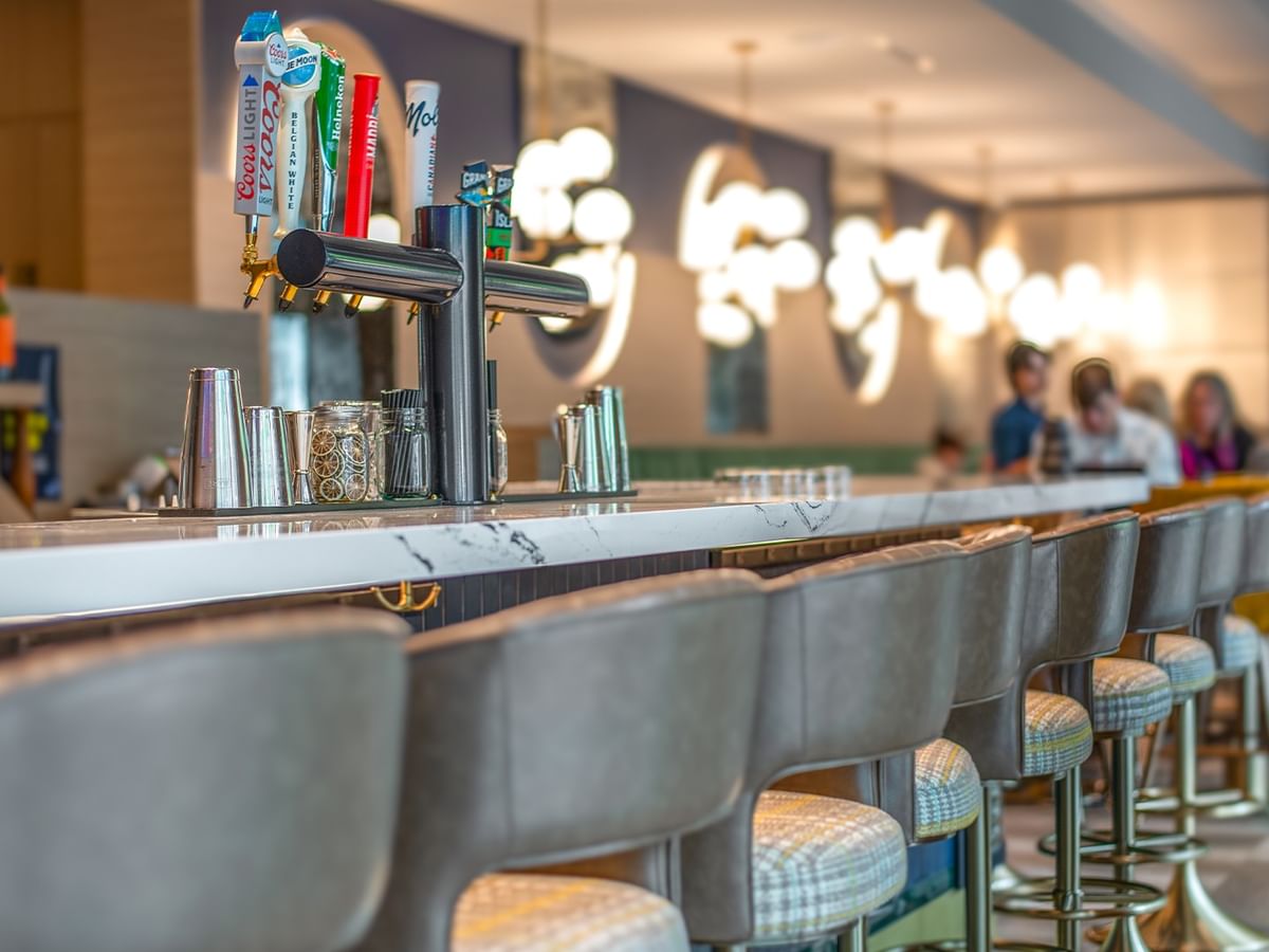 Bar with gray upholstered stools and taps .