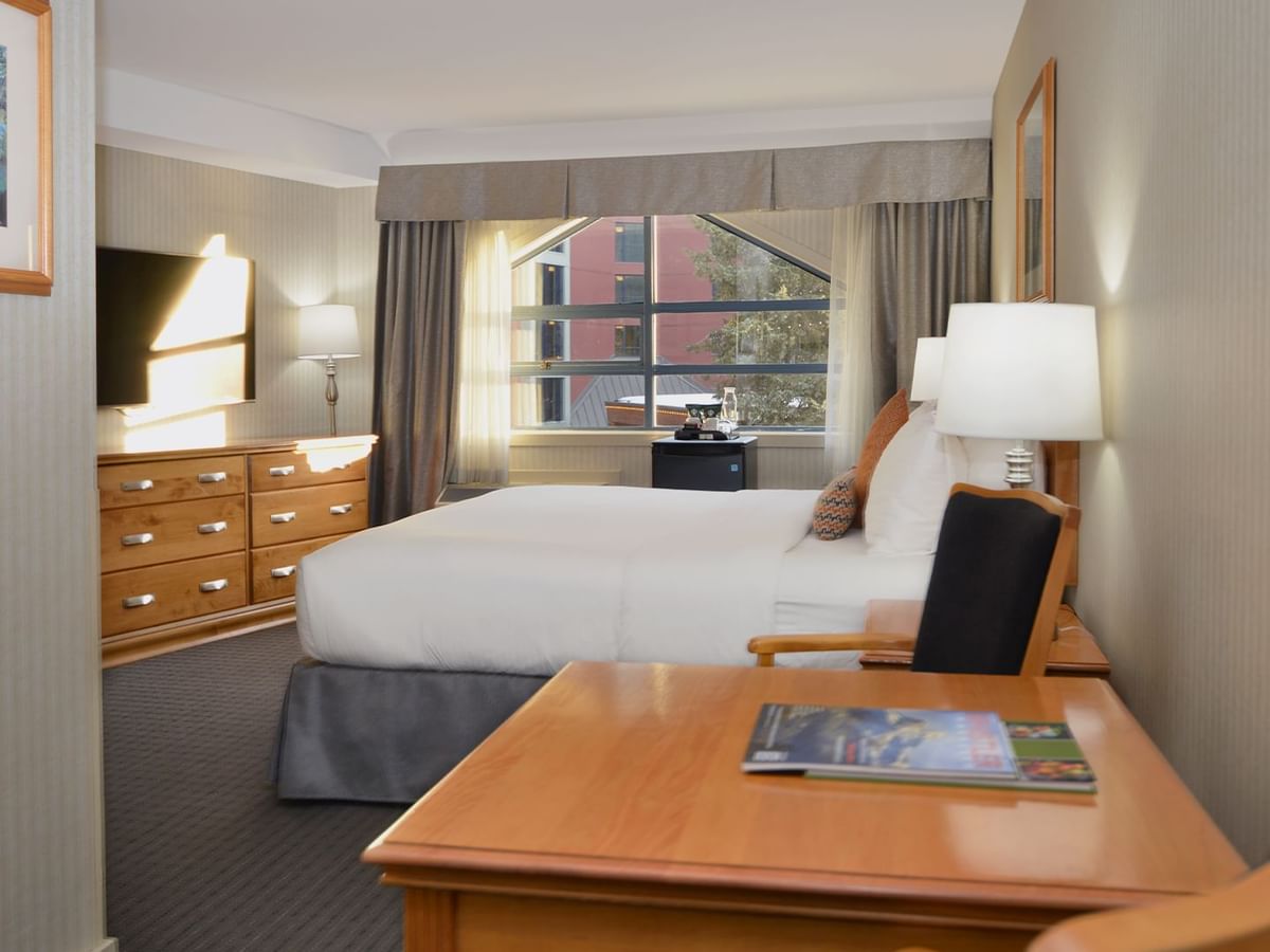 Spacious hotel room with a king bed, elegant decor and large window for natural light.