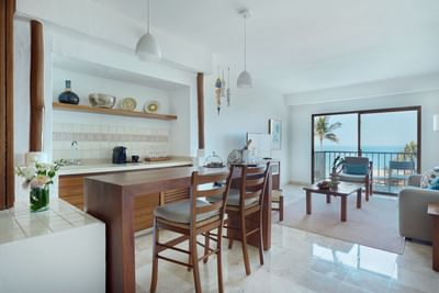 Living room with bar, chairs, balcony, and ocean view through large windows.