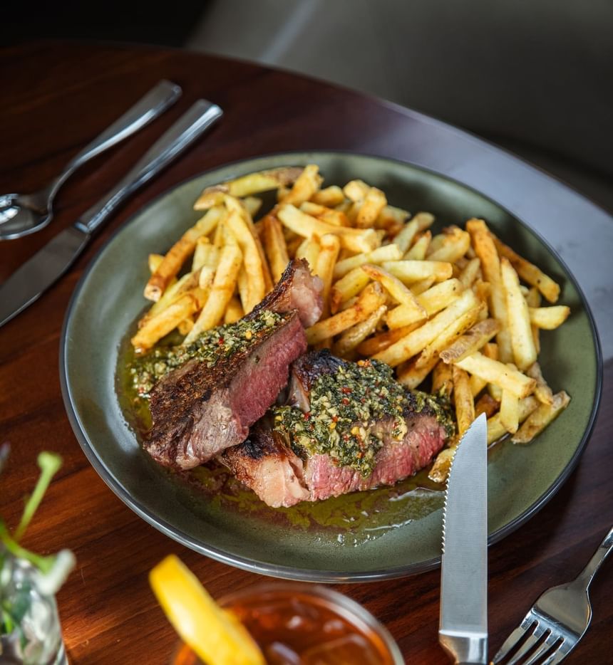Plate of crispy fries and herb-topped steak served with cocktail at Regency Restaurant in Portland Regency Hotel & Spa