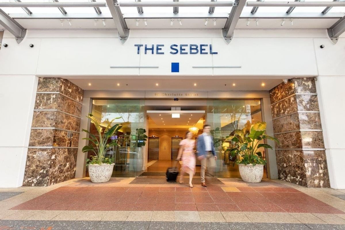Street-level entrance with marble accents, glass doors, and a couple checking into The Sebel Brisbane