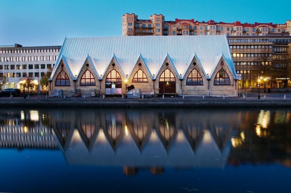 A building with a silver roof by a body of water at dusk with reflections in the water.