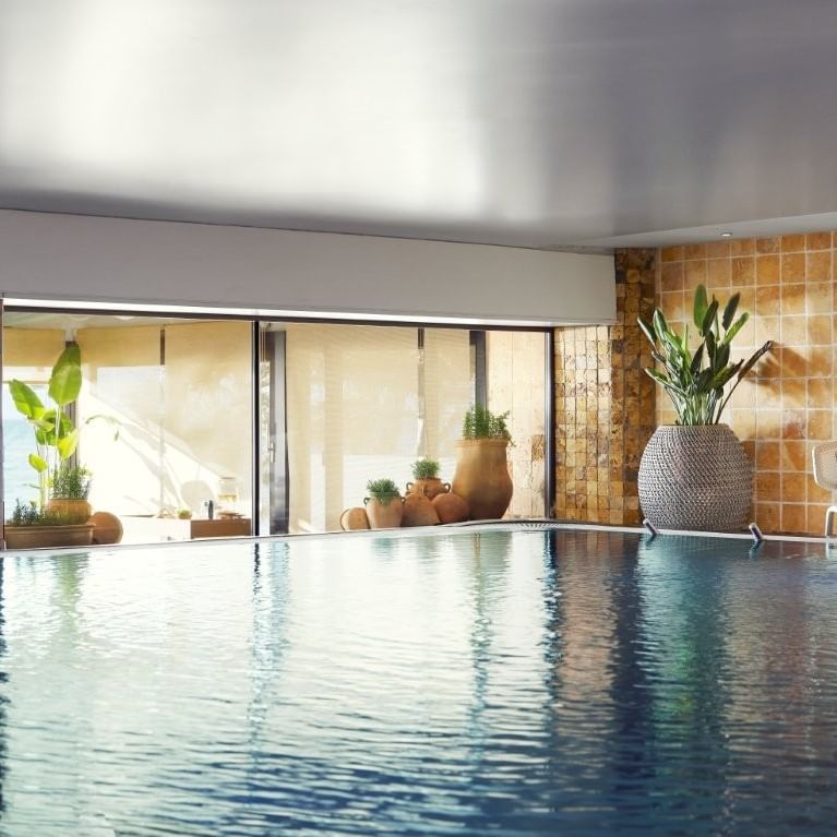 Piscina cubierta con vista al mar y decoración de plantas y sillas para la Experiencia de meditación en flotación