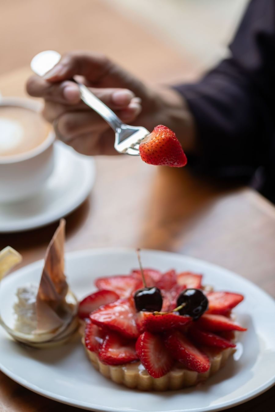 Hand holding a fork with a strawberry over a plate of cheesecake in Artist Lobby Lounge at Warwick Hotel Jeddah