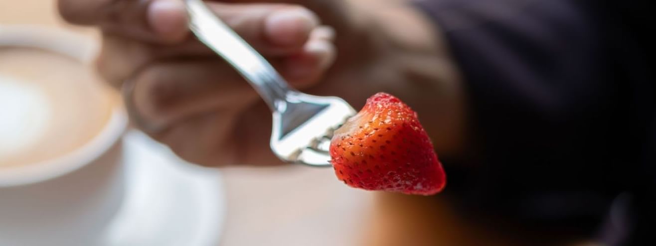 Hand holding a fork with a strawberry over a plate of cheesecake in Artist Lobby Lounge at Warwick Hotel Jeddah