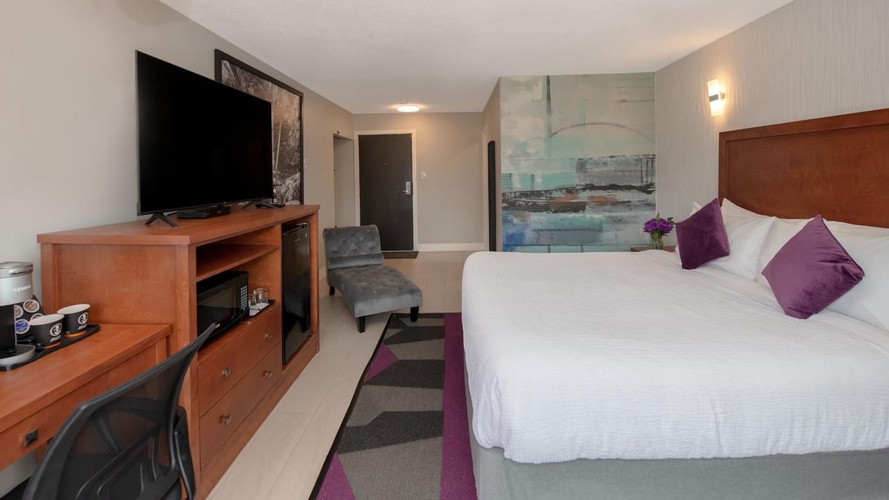 A hotel room with a bed, desk, chair, television and artwork on the wall.