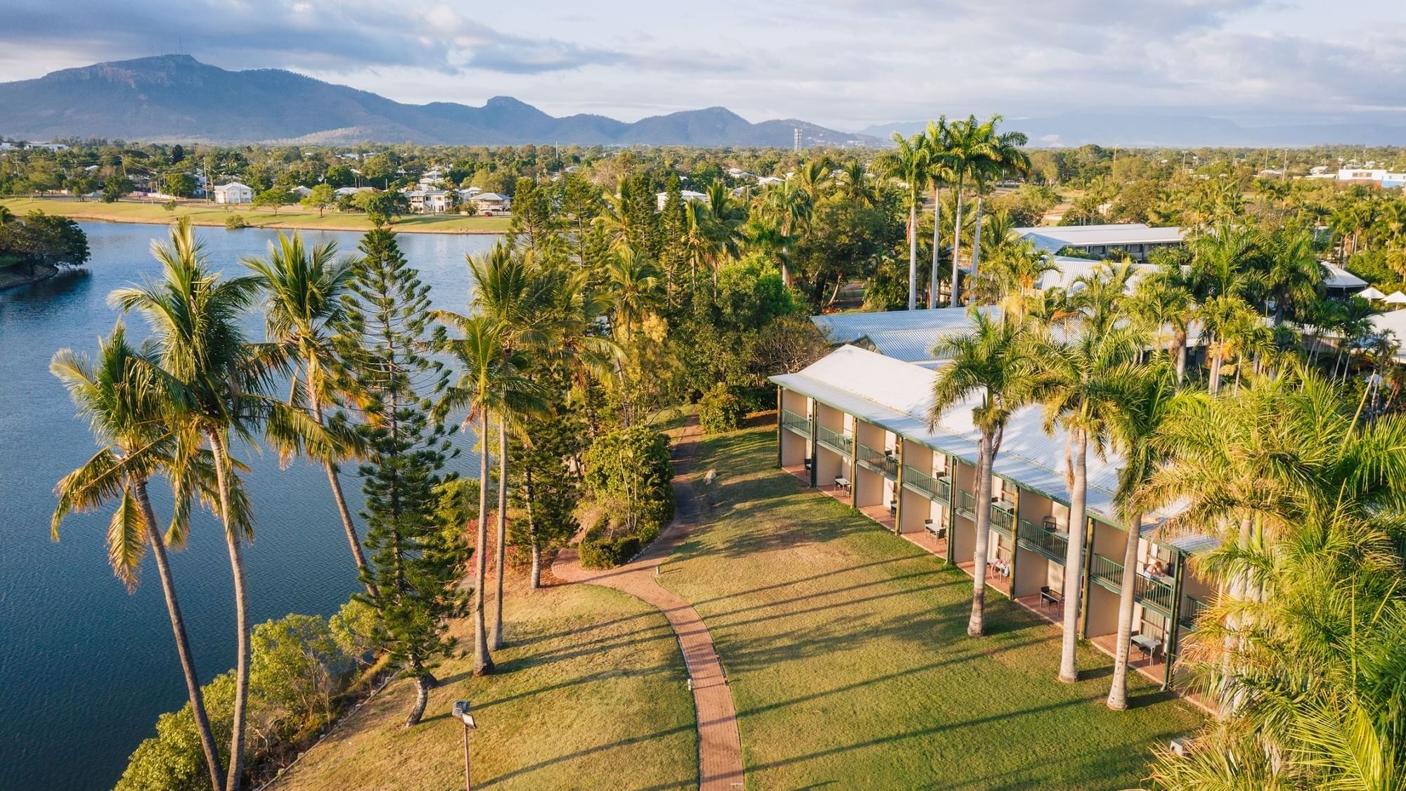 Aerial view of Mercure Hotel Townsville surrounded by palm trees, lush greenery and distant mountains