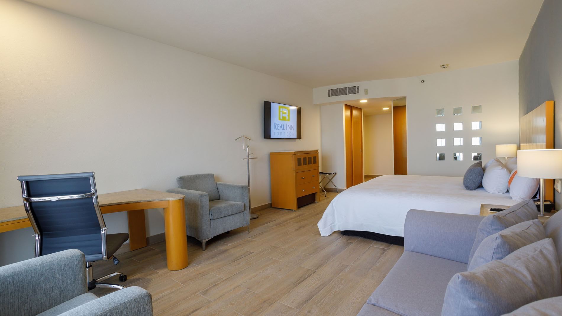 King Junior Suite with light wood floors, a grey sofa, and a sleek wooden work desk area at Real Inn Torreon
