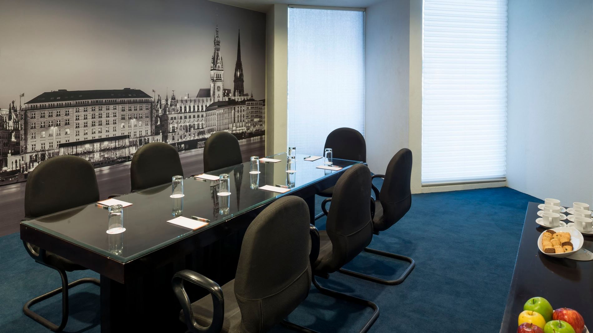 Meeting room featuring a glass table, black chairs, and a cityscape mural at Real Inn Nuevo Laredo