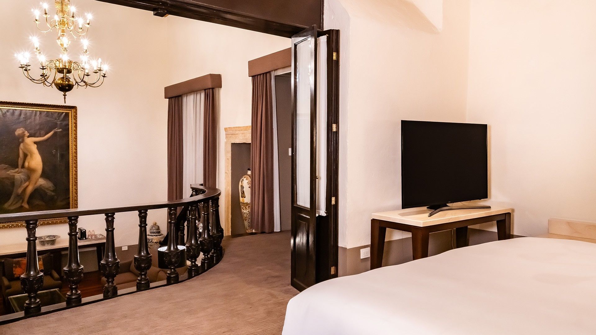 View from the King Presidential Suite toward a balcony with an ornate wood railing and a chandelier at Quinta Real Puebla