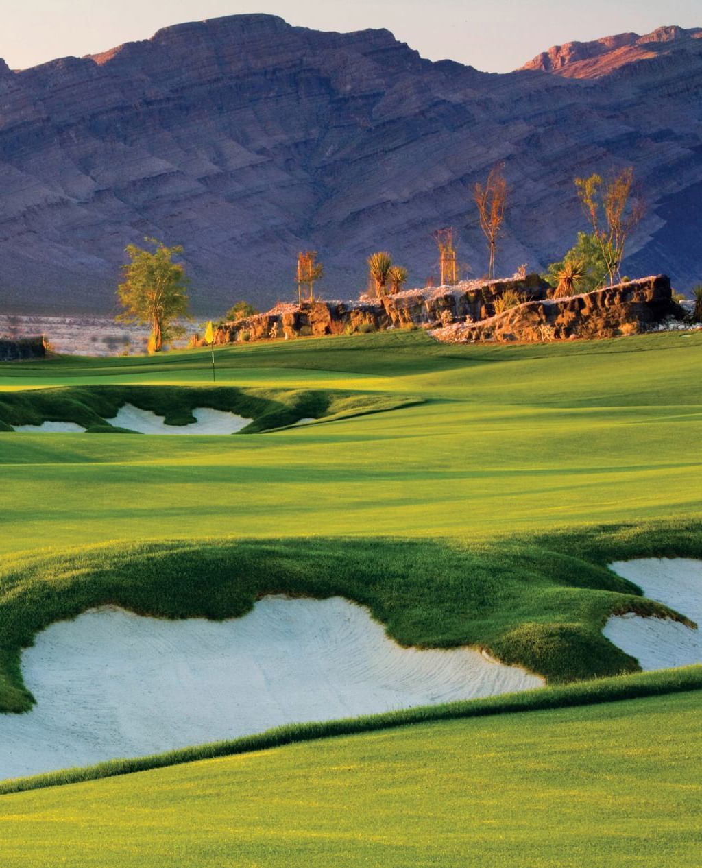 Lush green golf course with sand bunkers in front of majestic mountain ranges near Eureka Casino Resort