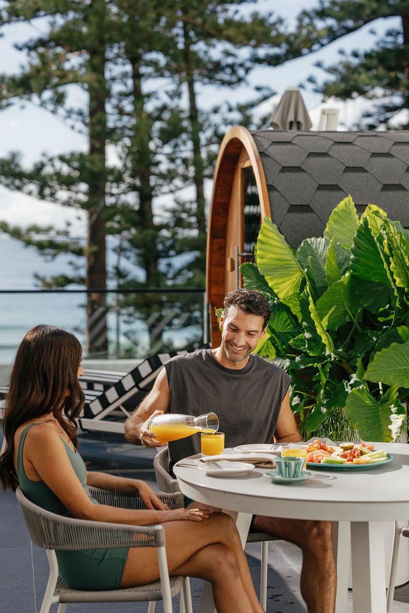 Elysium Manly outdoor patio at Manly Beach accommodation featuring a couple enjoying fresh orange juice by a sauna pod