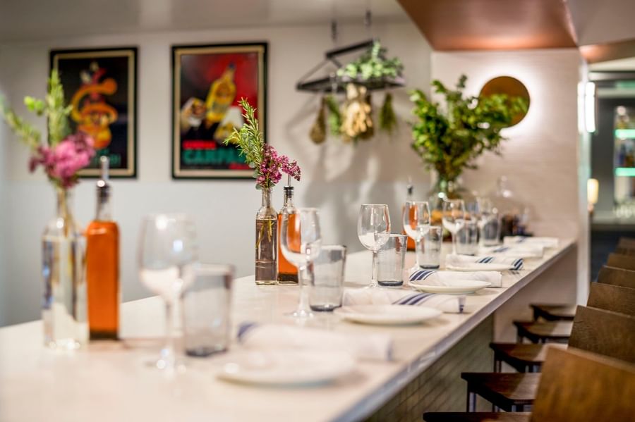Wine glasses and plates with oil bottles under dried herbs on a white bar counter in Ngattara-Restaurant at Warwick Denver