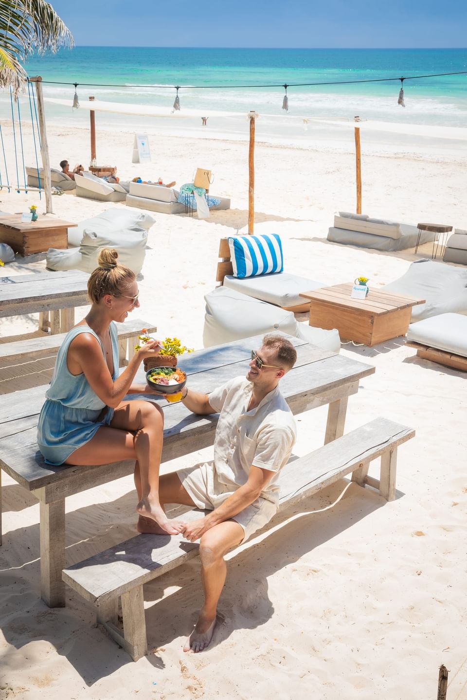 A happy couple enjoys a beautiful outdoor lunch on wooden benches near the turquoise water at La Zebra Hotel