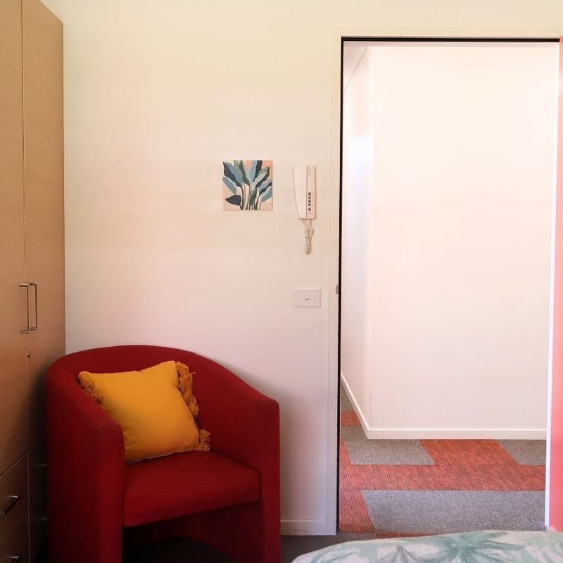 Red chair with a yellow pillow beside an open red door at La Trobe University Hillside Apartments.