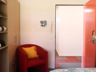 Red chair with a yellow pillow beside an open red door at La Trobe University Hillside Apartments.
