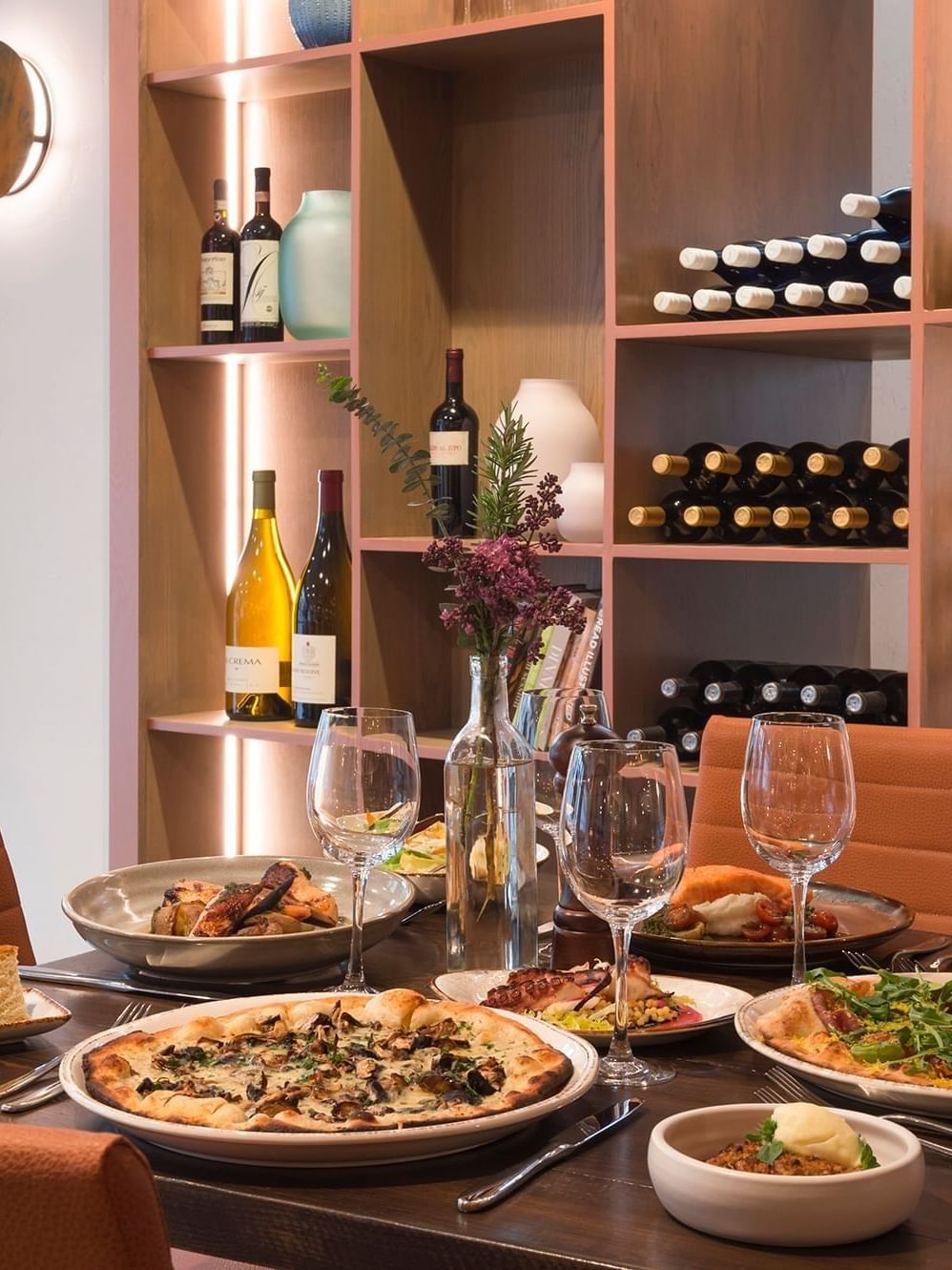 Pizzas and wine on a table by a wooden shelving unit filled with bottles at Warwick Denver
