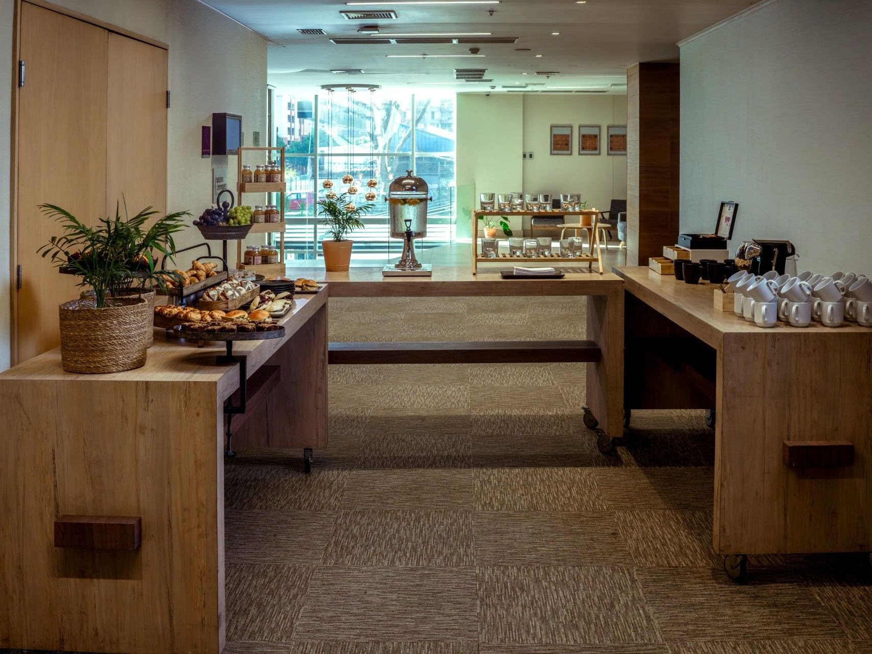 Mesas de bufé de madera con comida y tazas de café en el vestíbulo de un hotel.