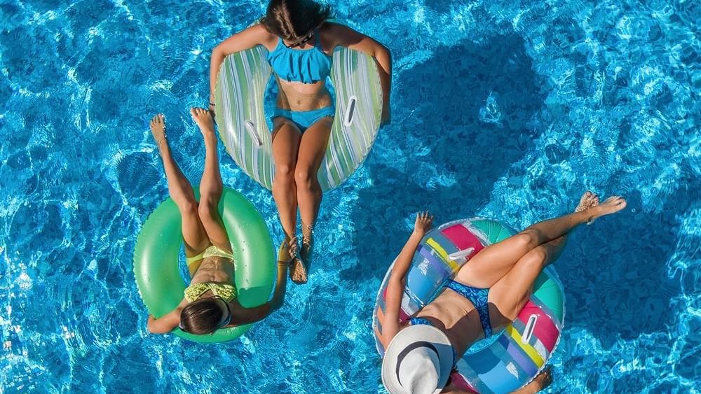 Three women relaxing on inflatable floats in a swimming pool.