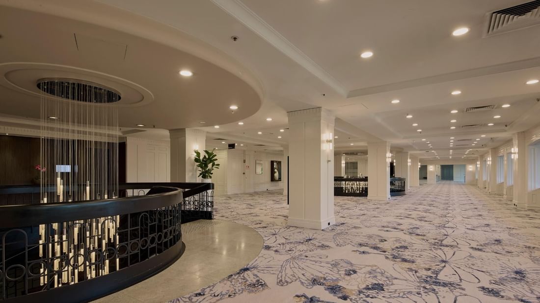 Spacious conference foyer with patterned carpet, modern chandelier, and white columns at Pullman East Melbourne.