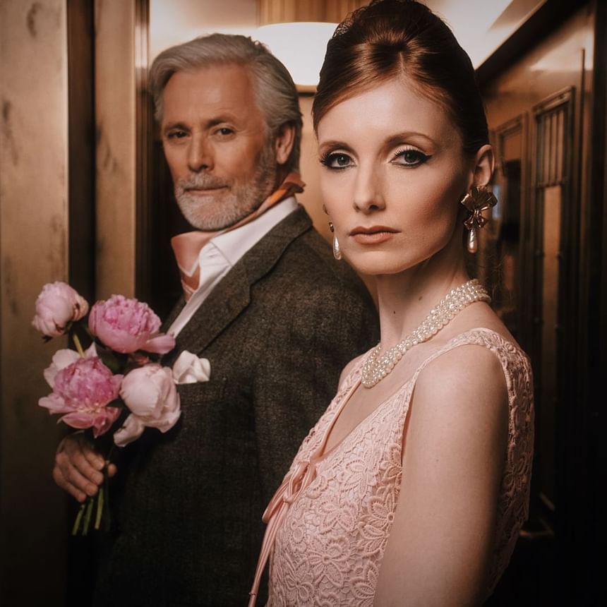 Man with peonies and a woman in pink lace and pearls standing stylishly in an elevator at Hotel Motto Vienna