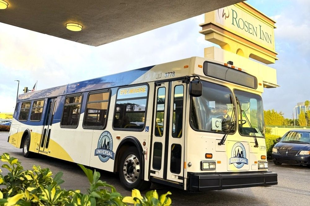The front and side of one of the complimentary shuttle buses to Universal theme parks from Rosen Inn, with the Rosen Inn sign in the background.