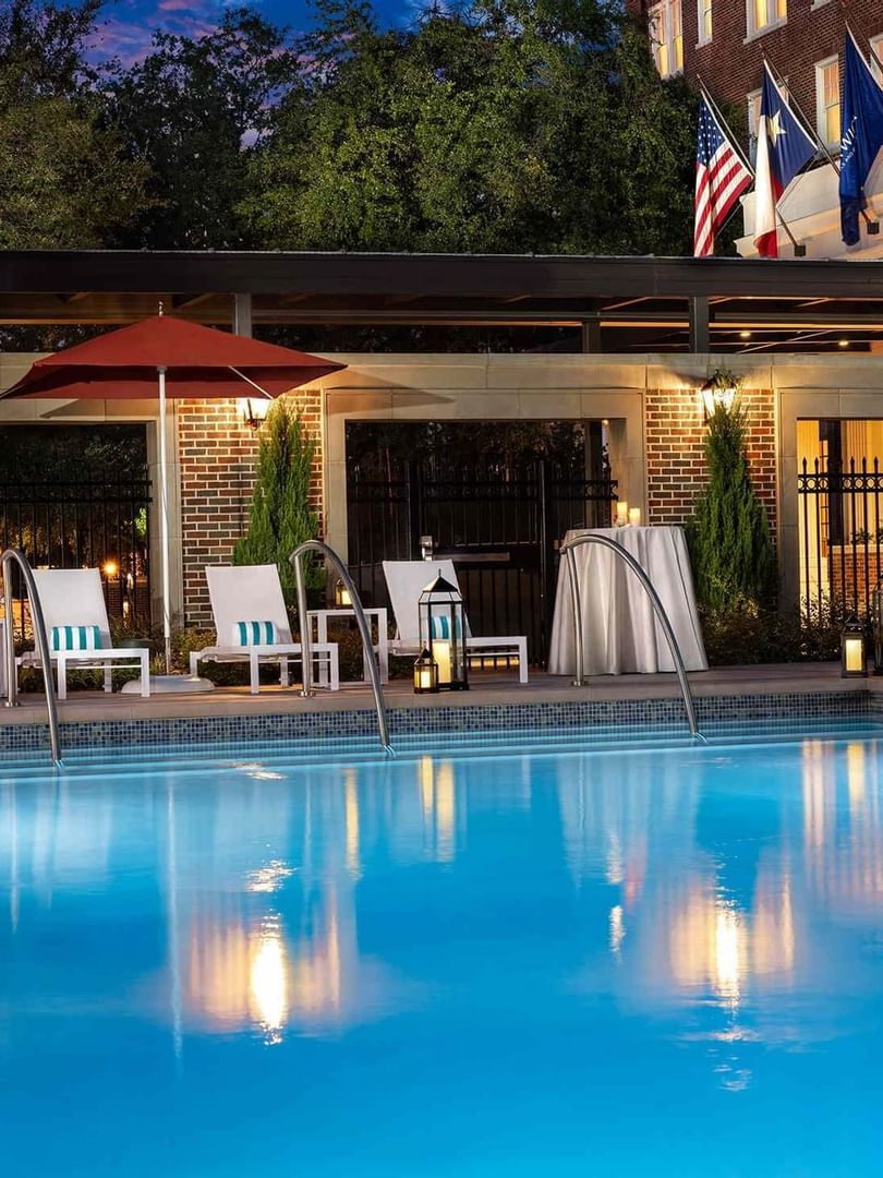Blue pool by lounge chairs under a red umbrella at Warwick Melrose Dallas