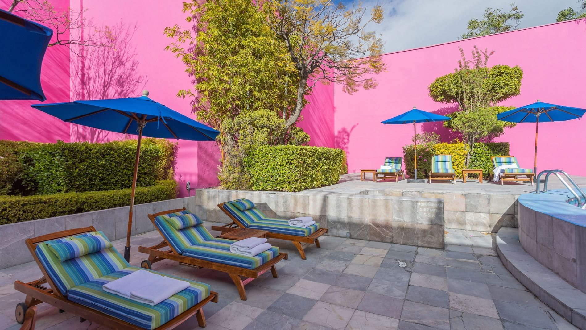 Patio exterior en Suite King Fiesta con sombrillas azules y tumbonas junto a muros rosas en Camino Real Polanco México