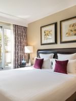White bed with burgundy pillows by a side table in Executive Suite with Terrace art at Warwick Paris Champs Elysées