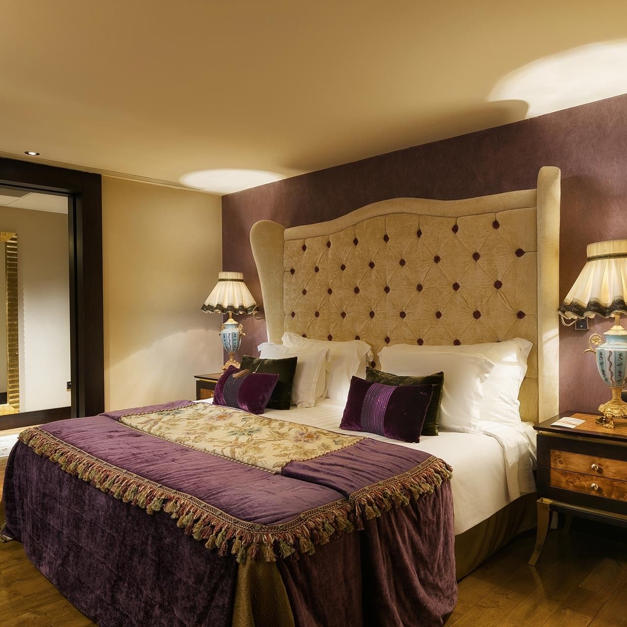Elegant bedroom with large bed, purple bedding, wooden floors, and ornate nightstands with lamps in Pool Duplex Suite at Titanic Mardan Palace.