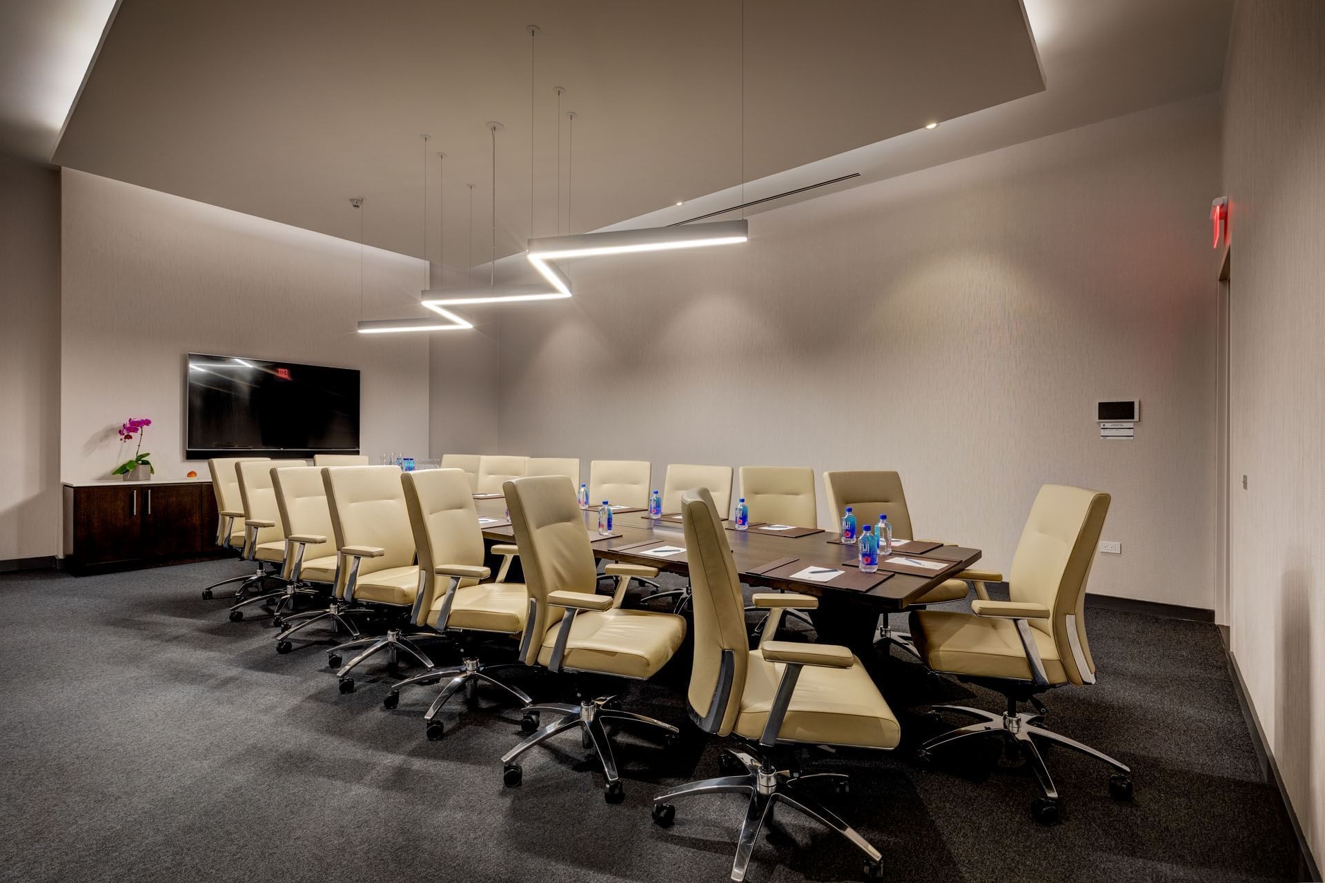Champion\'s Boardroom with beige leather chairs facing TV screen beside a modern zig-zag light fixture at Hotel X Toronto