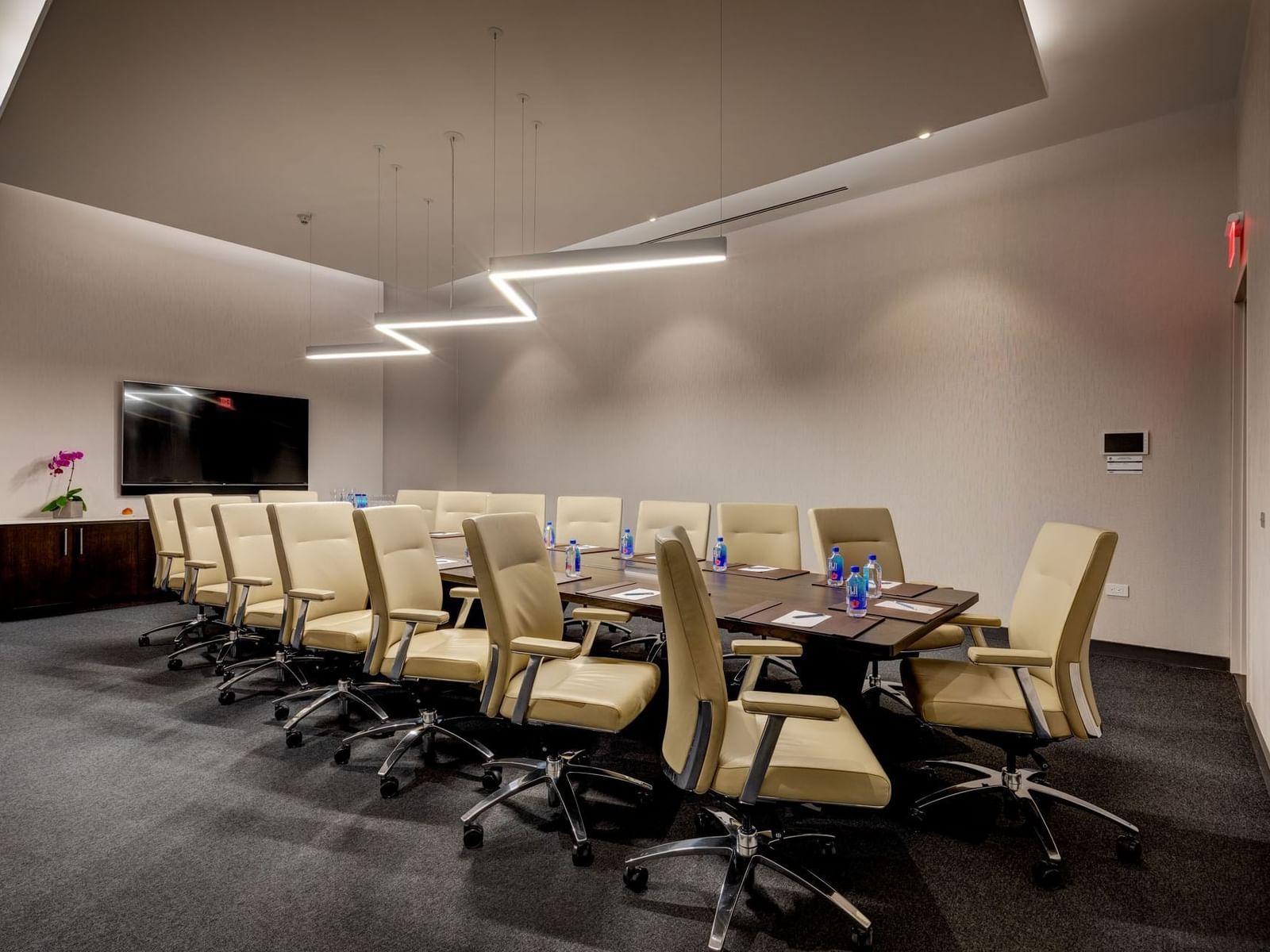 Champion's Boardroom with a large table, beige chairs, a TV, and unique lighting fixtures at Hotel X Toronto