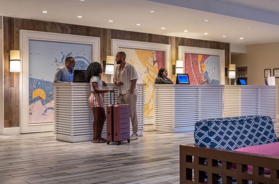 Guests by white reception desks under colorful art and warm lights in the Reception at Warwick Paradise Island Bahamas