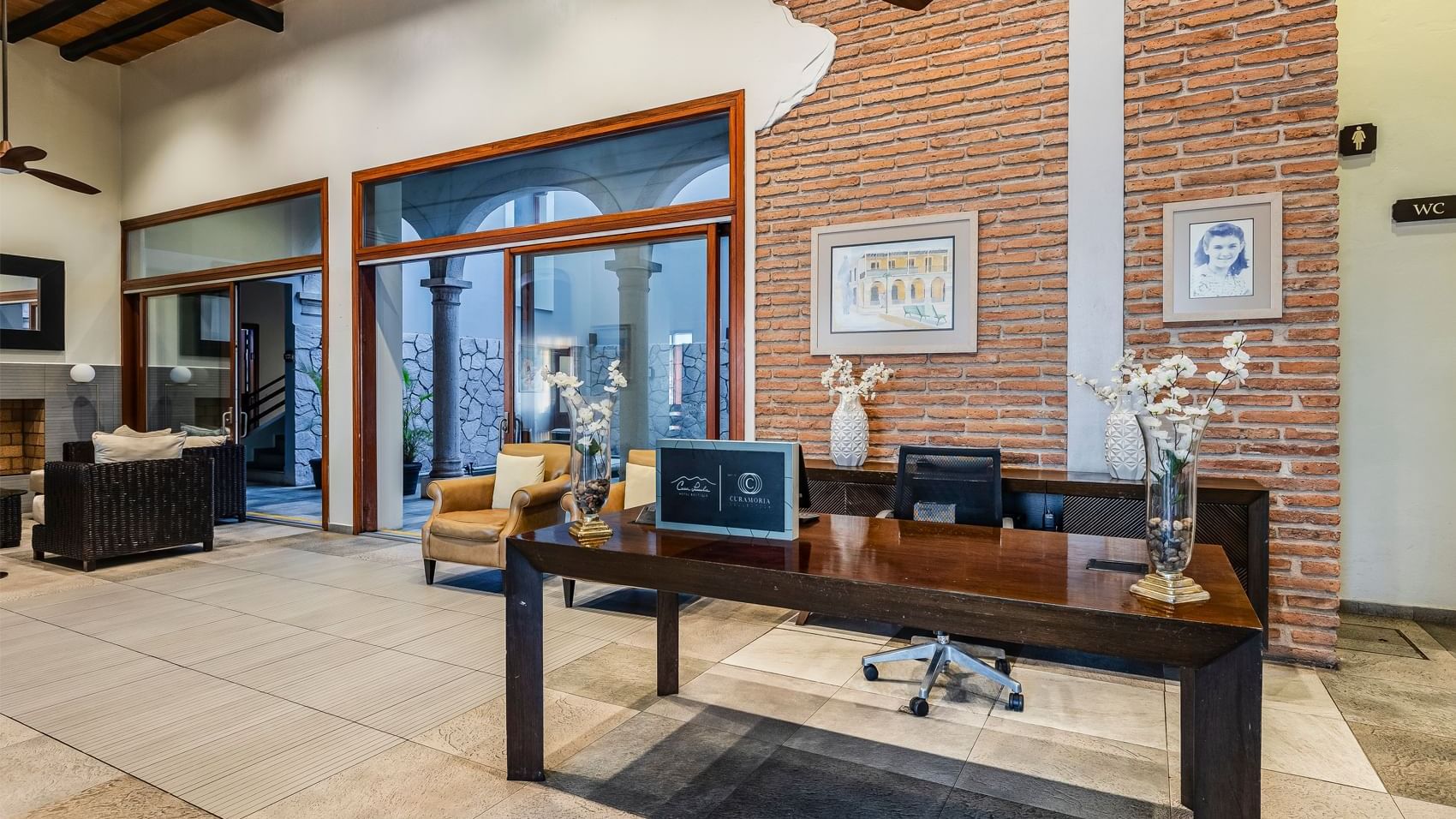 Elegant lobby featuring a wooden desk, brick accent wall, and classic decor at Curamoria Collection