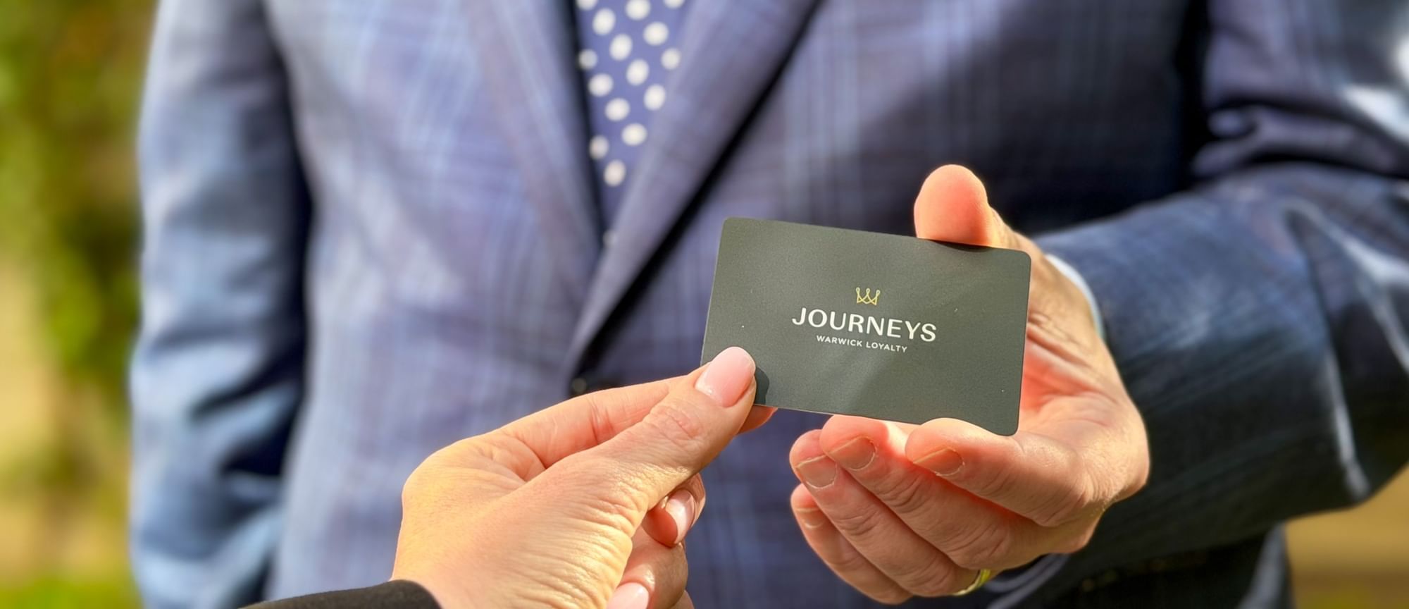 Hand holding a Journeys Warwick Loyalty card by a professional suit at The Capital Hotel, Apartments and Townhouse