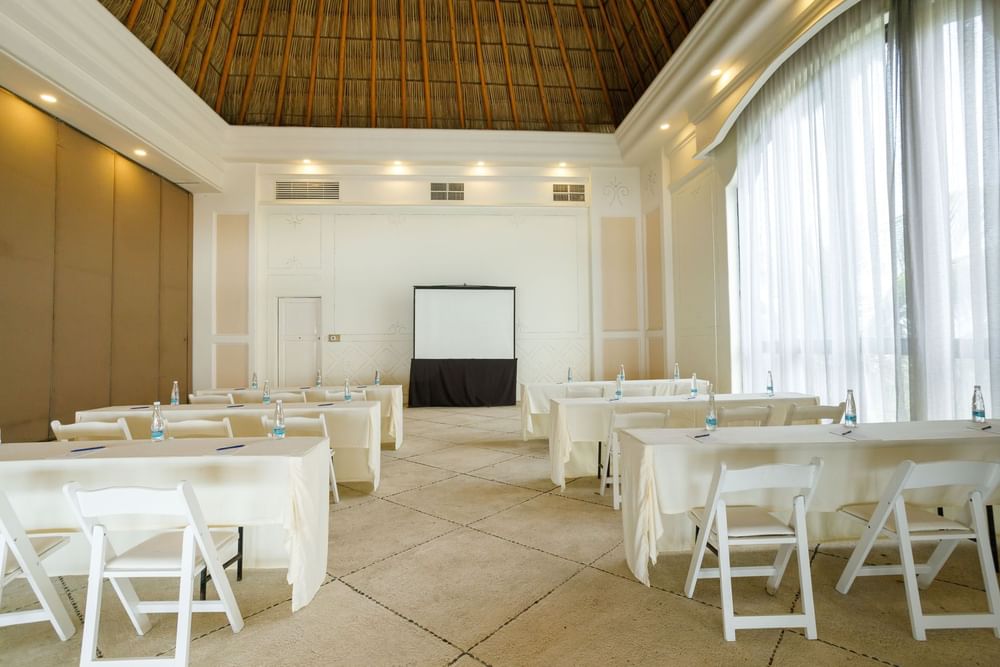 Bright classroom style Ixtac Venue with rows of tables and a projection screen at Quinta Real Acapulco