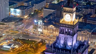 Aerial night view of a bustling city intersection with a clock tower and surrounding buildings near Polonia Palace Hotel