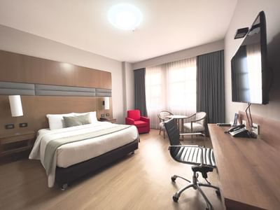 Business Carlton Queen featuring a king bed, workspace, TV, red armchair, and a small table at Dann Carlton Cali