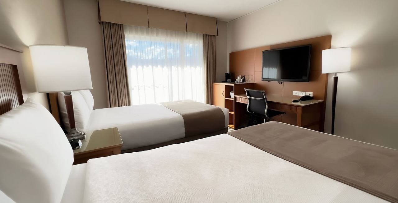 Hotel room with two beds, TV, work desk, chair, and window