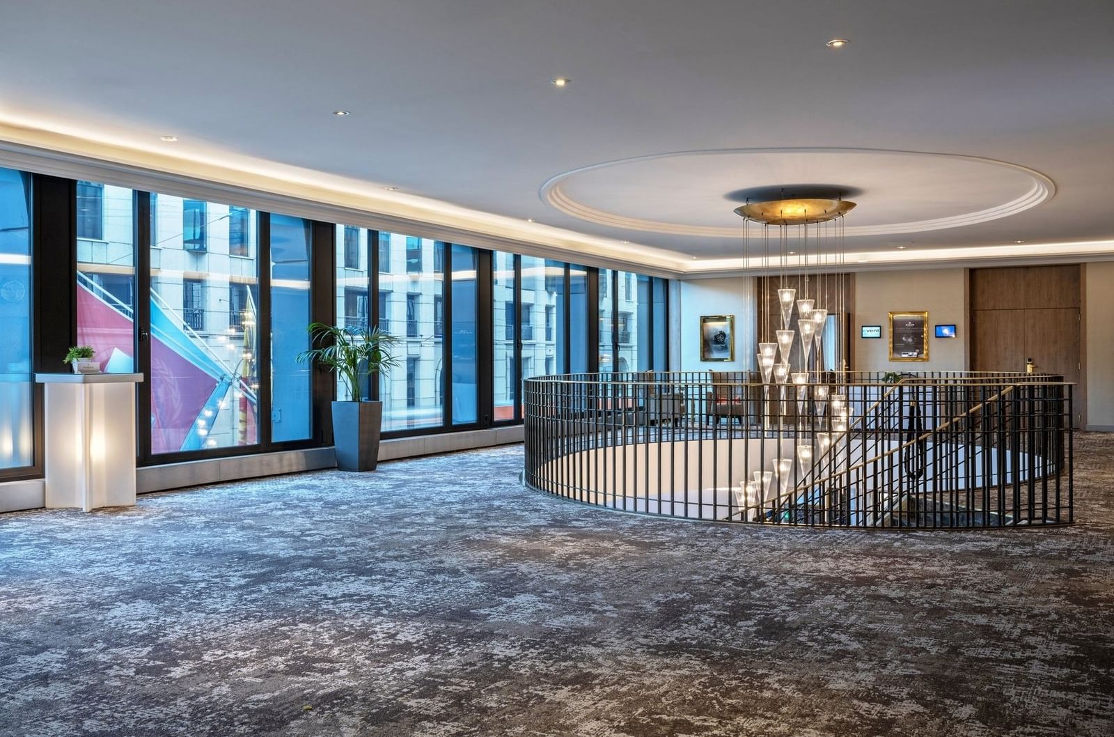 Spiral staircase by large windows under a tiered glass chandelier in Foyer Mezzanine at Warwick Geneva