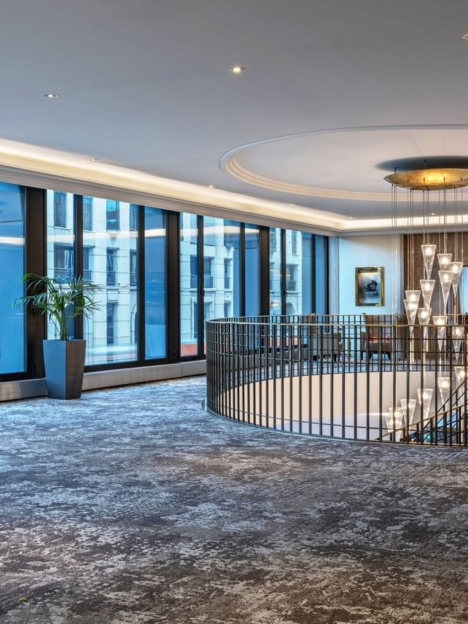 Spiral staircase by large windows under a tiered glass chandelier in Foyer Mezzanine at Warwick Geneva