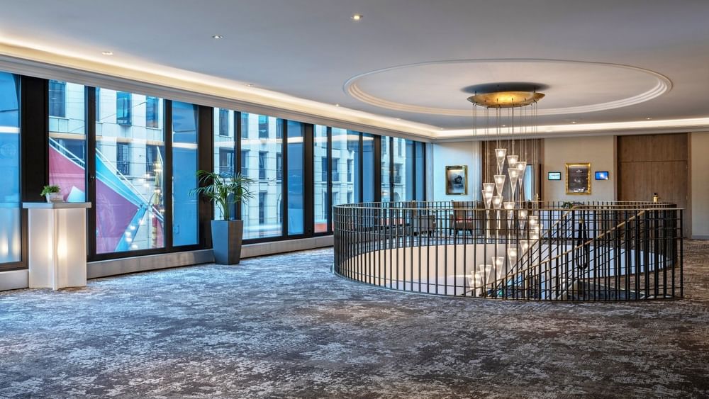 Spiral staircase by large windows under a tiered glass chandelier in Foyer Mezzanine at Warwick Geneva